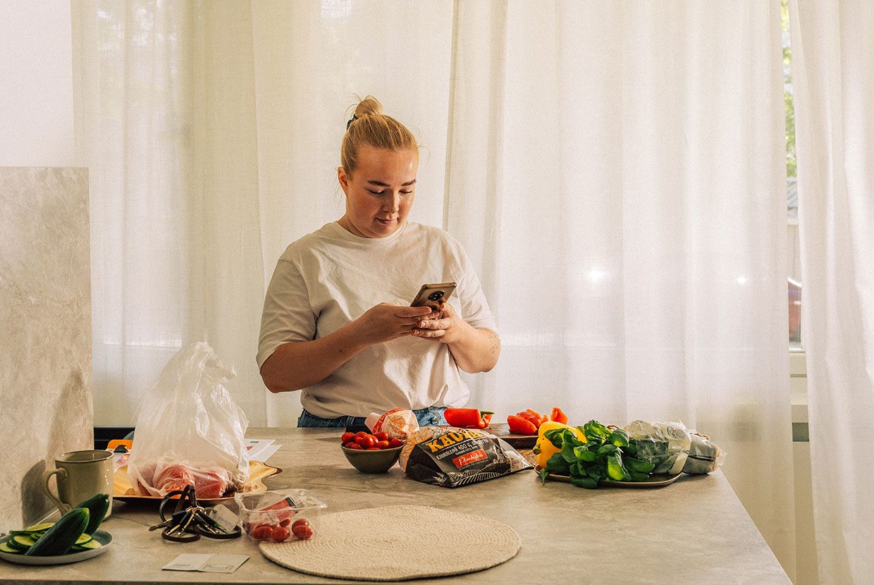 Henkilö pitää kädessään matkapuhelinta ja seisoo leipätarvikkeilla katetun pöydän takana. Porokylän Leipomon sosiaalinen media ja sisällöntuotanto rakentuu Huhu Digitalin suunnittelemana ja toteuttamana.