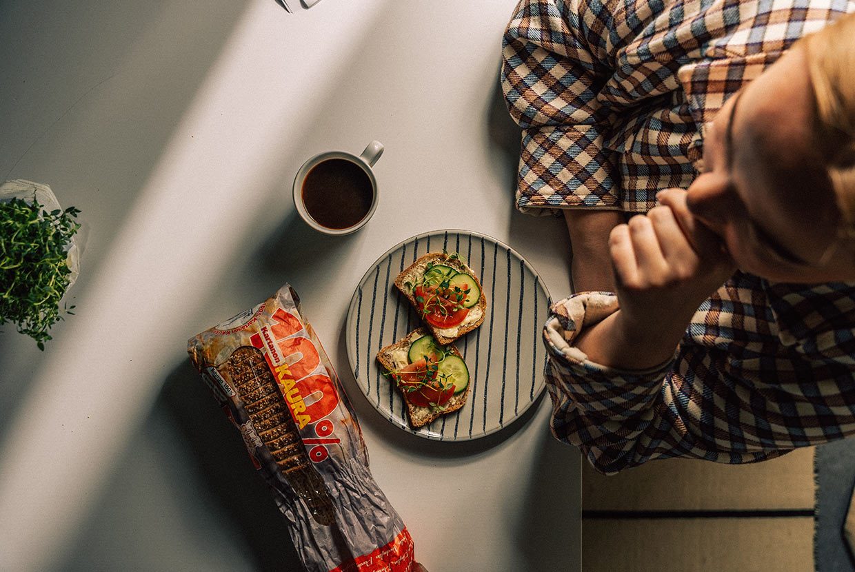 Henkilö istuu pöydän ääressä. Pöydällä on leipäpussi, täytetyt eväsleivät ja kahvikuppi. Porokylän Leipomon sosiaalinen media ja sisällöntuotanto rakentuu Huhu Digitalin suunnittelemana ja toteuttamana.